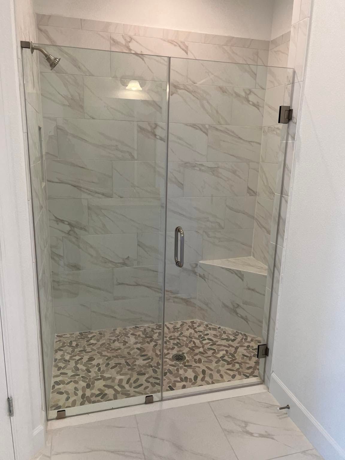 Frameless hinged glass shower door with matte black hardware in a marble tiled Tampa bathroom
